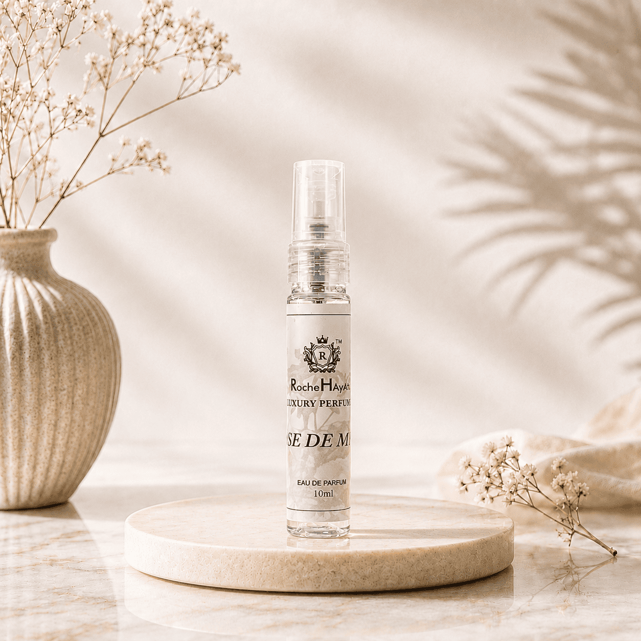 RocheHayatt Rose De Musk 10ml Eau De Parfum travel spray bottle displayed on a cream marble podium with a soft beige floral background, creating a luxurious and elegant product presentation.